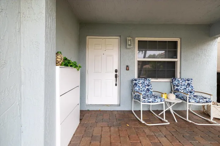 Covered entryway featuring a white paneled door, exterior wall light fixture, and a window with horizontal blinds