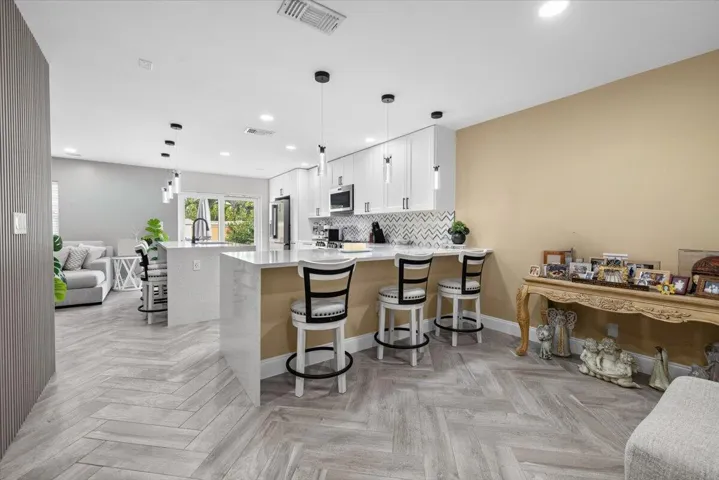 Open-concept kitchen featuring white shaker cabinetry, an island with seating, pendant lighting, and a patterned tile backsplash