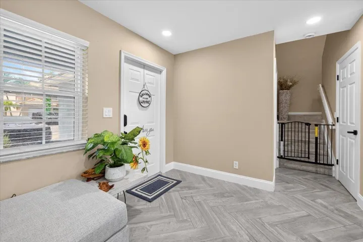 Entryway featuring herringbone-patterned wood-finish flooring, a white paneled door with black hardware, and an adjacent window with white blinds