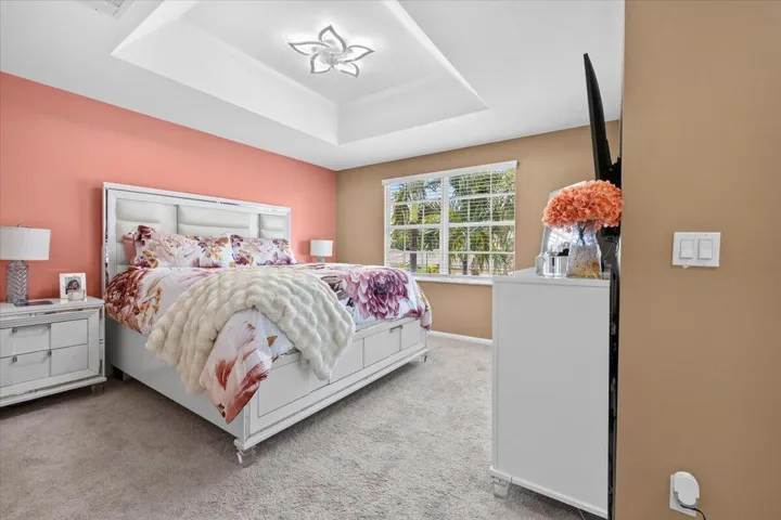 Spacious room featuring a tray ceiling with a modern light fixture, a wide window with horizontal blinds, and soft carpet flooring