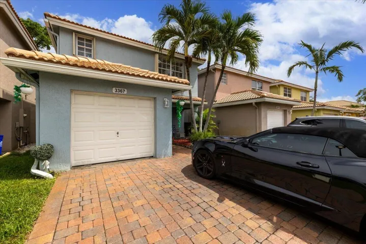 Residence featuring a light blue stucco exterior, single-car garage, and a paver driveway