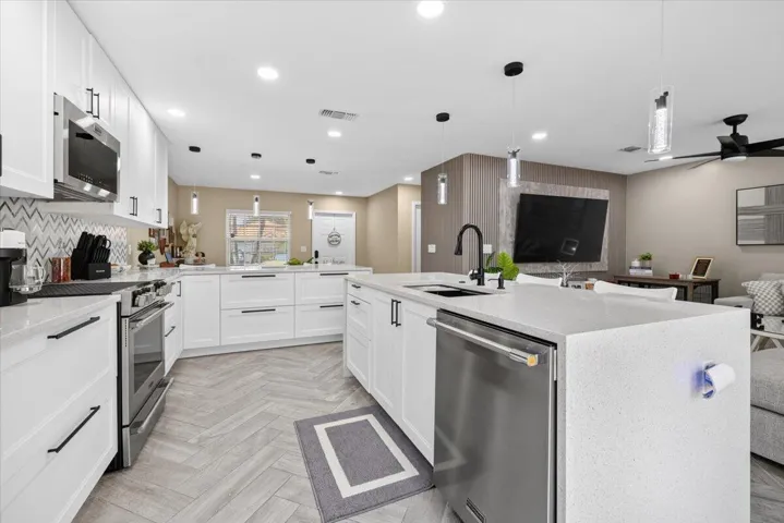 Open-concept kitchen featuring white cabinetry, stainless steel appliances, a large island with sink, herringbone-patterned flooring, and recessed lighting