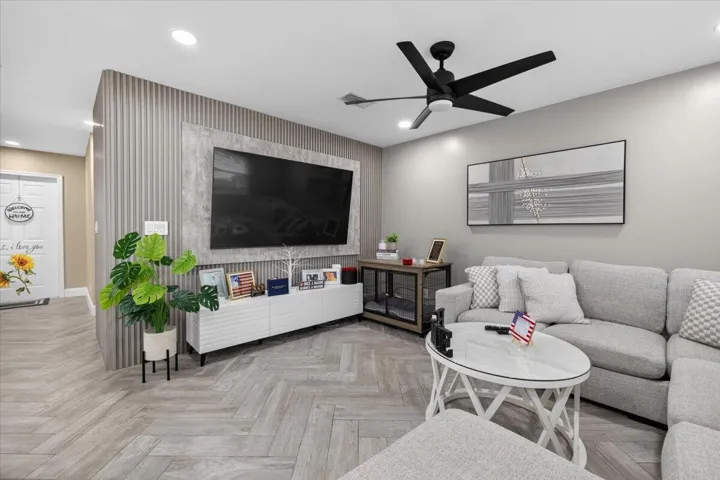 Living area featuring wood-finish flooring in a herringbone pattern, a contemporary ceiling fan, recessed lighting, and a textured accent wall with a built-in media center