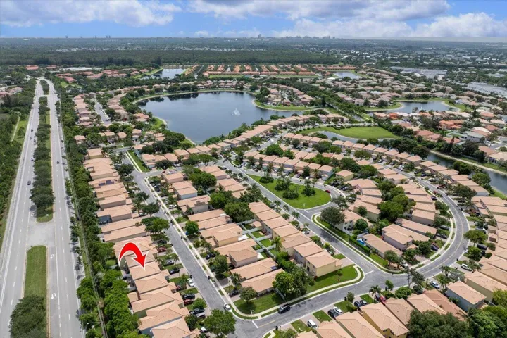 Aerial perspective of a structured community featuring numerous residential properties with light-colored tile roofs, a large central lake, and multiple curving streets