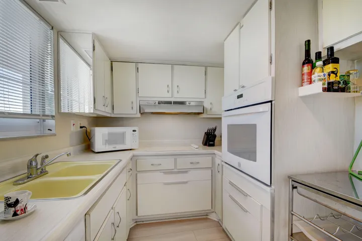 Kitchen featuring white cabinetry, light-toned countertops, a dual basin sink, integrated wall oven, and wood-finish flooring