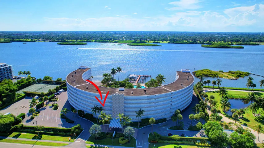 Curved architectural design building with multiple stories, waterfront location, onsite swimming pool, tennis courts, and mature palm tree landscaping