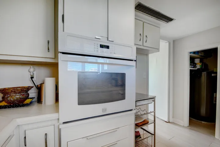 Built-in wall oven with white cabinetry, light countertops, and light wood-finish flooring