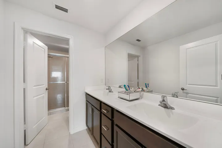 Bathroom featuring a dual vanity with dark wood-finish cabinetry, white countertops, and a full-width mirror
