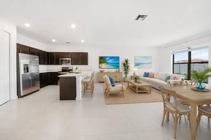Open-concept living space featuring a kitchen with dark cabinetry, stainless steel appliances, a snack bar with seating, a dining area, and a living area with large windows