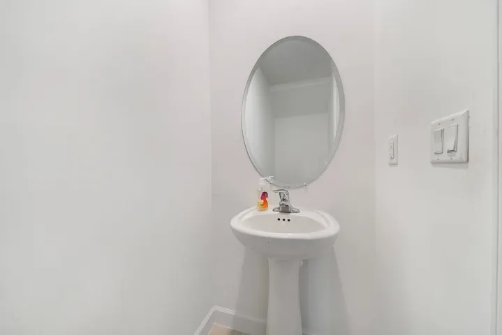 Pedestal sink with chrome faucet, complemented by an oval wall-mounted mirror