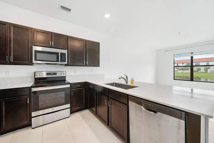 Kitchen featuring dark wood cabinetry, light-toned countertops, snack bar, stainless steel appliances, pantry, and recessed lighting