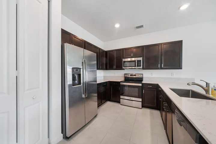 Kitchen featuring dark wood cabinetry, light-toned countertops, snack bar, stainless steel appliances, pantry, and recessed lighting