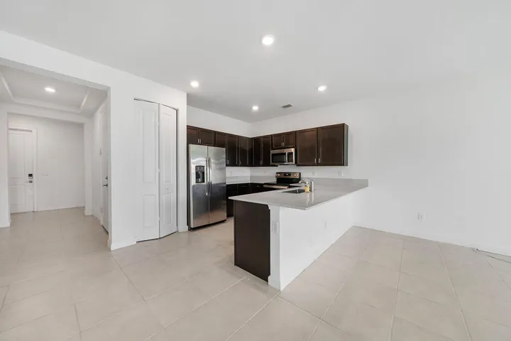 Kitchen featuring dark wood cabinetry, light-toned countertops, snack bar, stainless steel appliances, pantry, and recessed lighting