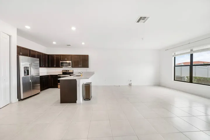 Open-concept living area featuring a kitchen with dark wood cabinetry, stainless steel appliances, and a snack bar