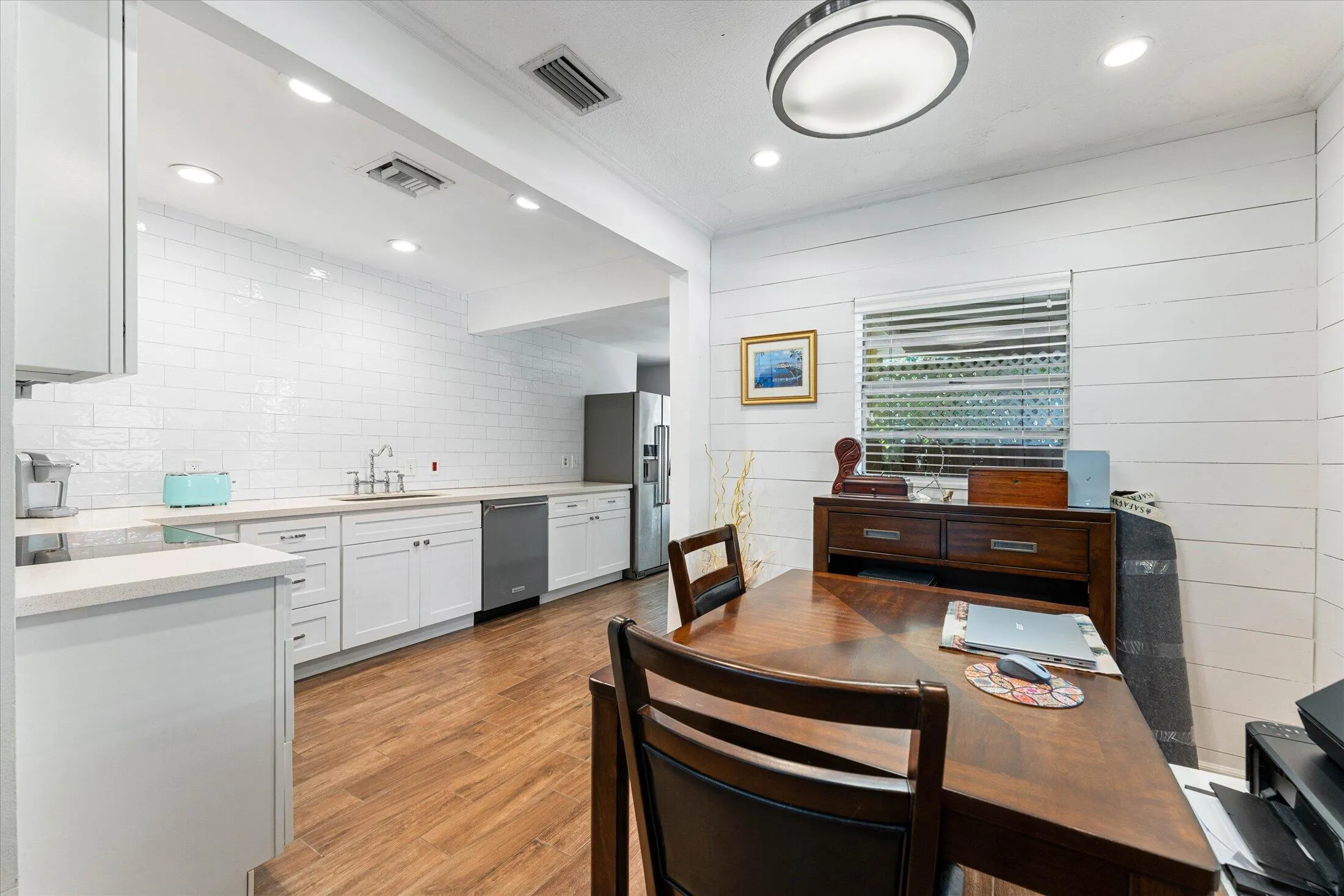 Kitchen and dining area featuring wood-finish flooring, white subway tile backsplash, white shaker cabinetry, and recessed lighting
