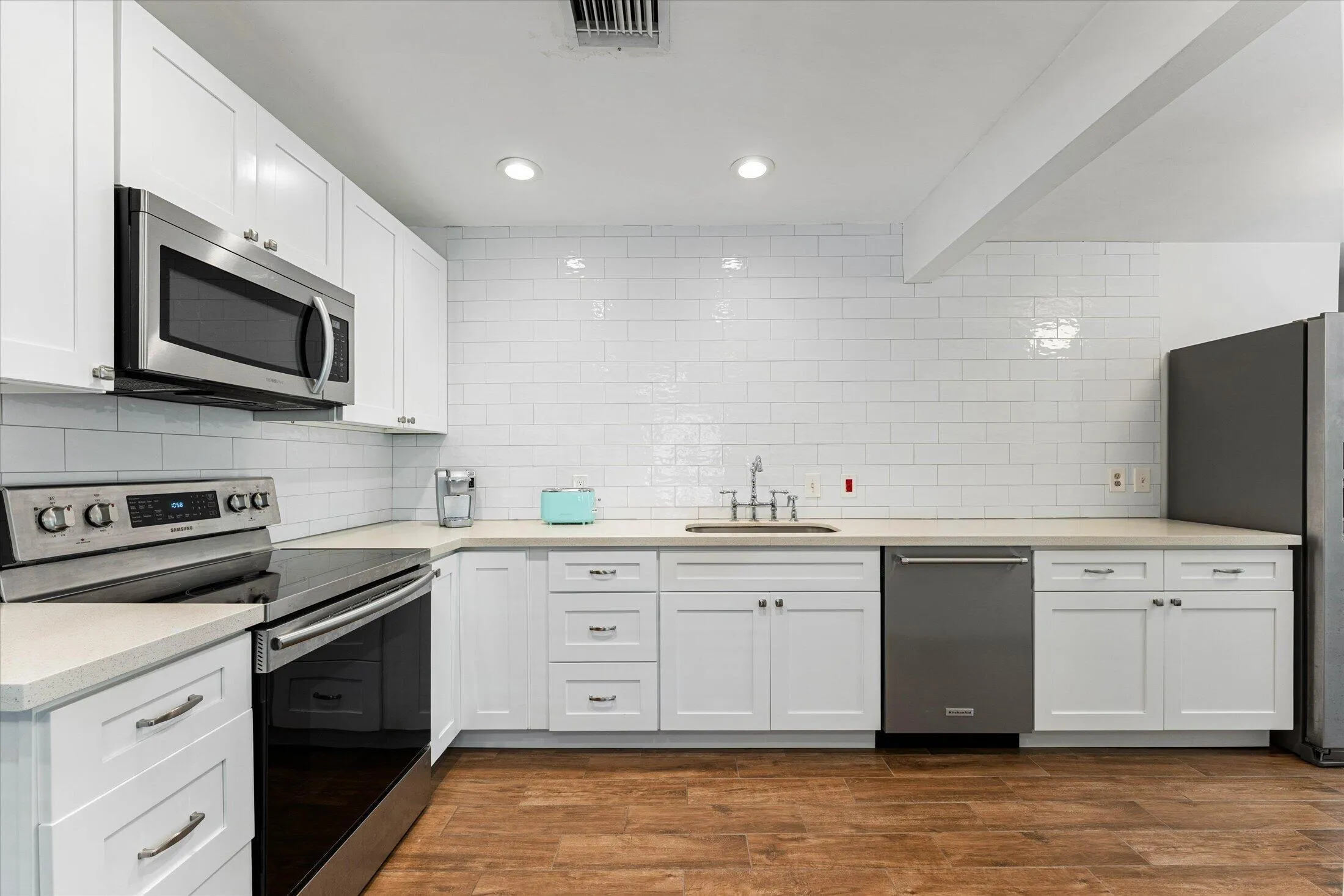 U-shaped kitchen featuring white shaker cabinetry, stainless steel appliances, light-toned countertops, a white subway tile backsplash, and wood-finish flooring
