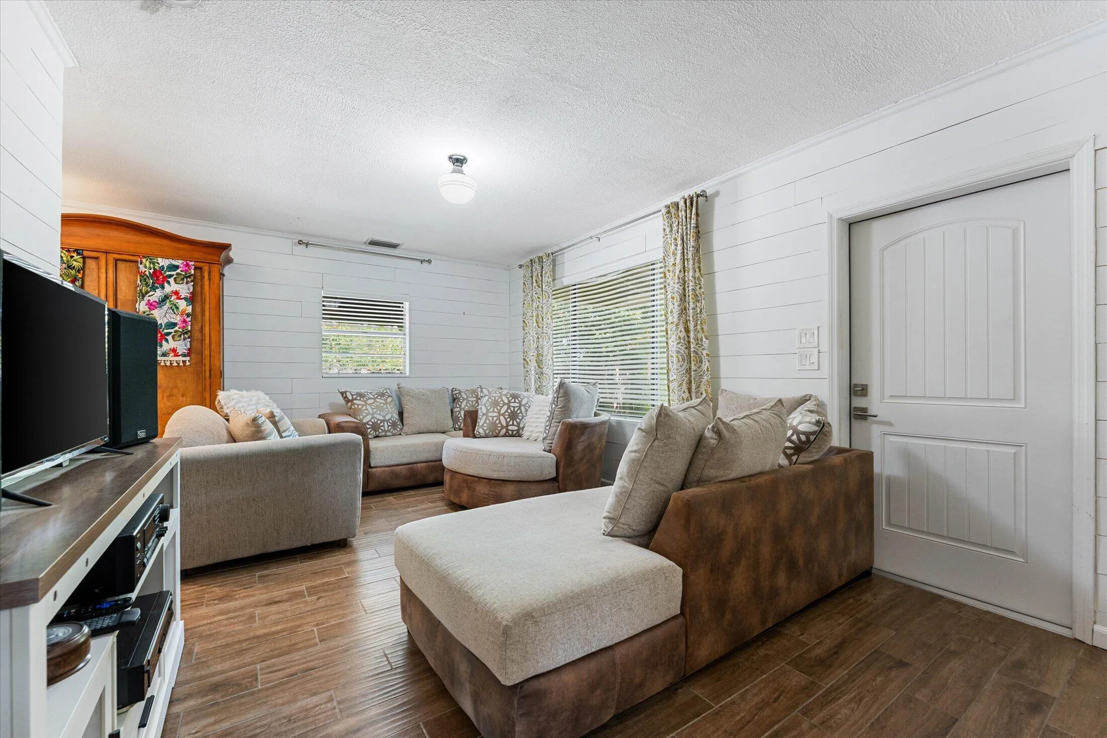 Interior living space featuring wood-finish flooring, white shiplap walls, and multiple windows with blinds