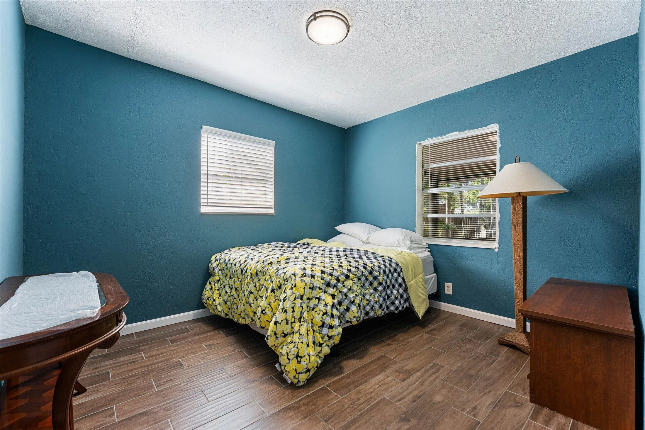 Spacious room featuring wood-finish flooring, two windows with blinds, and a built-in ceiling light fixture