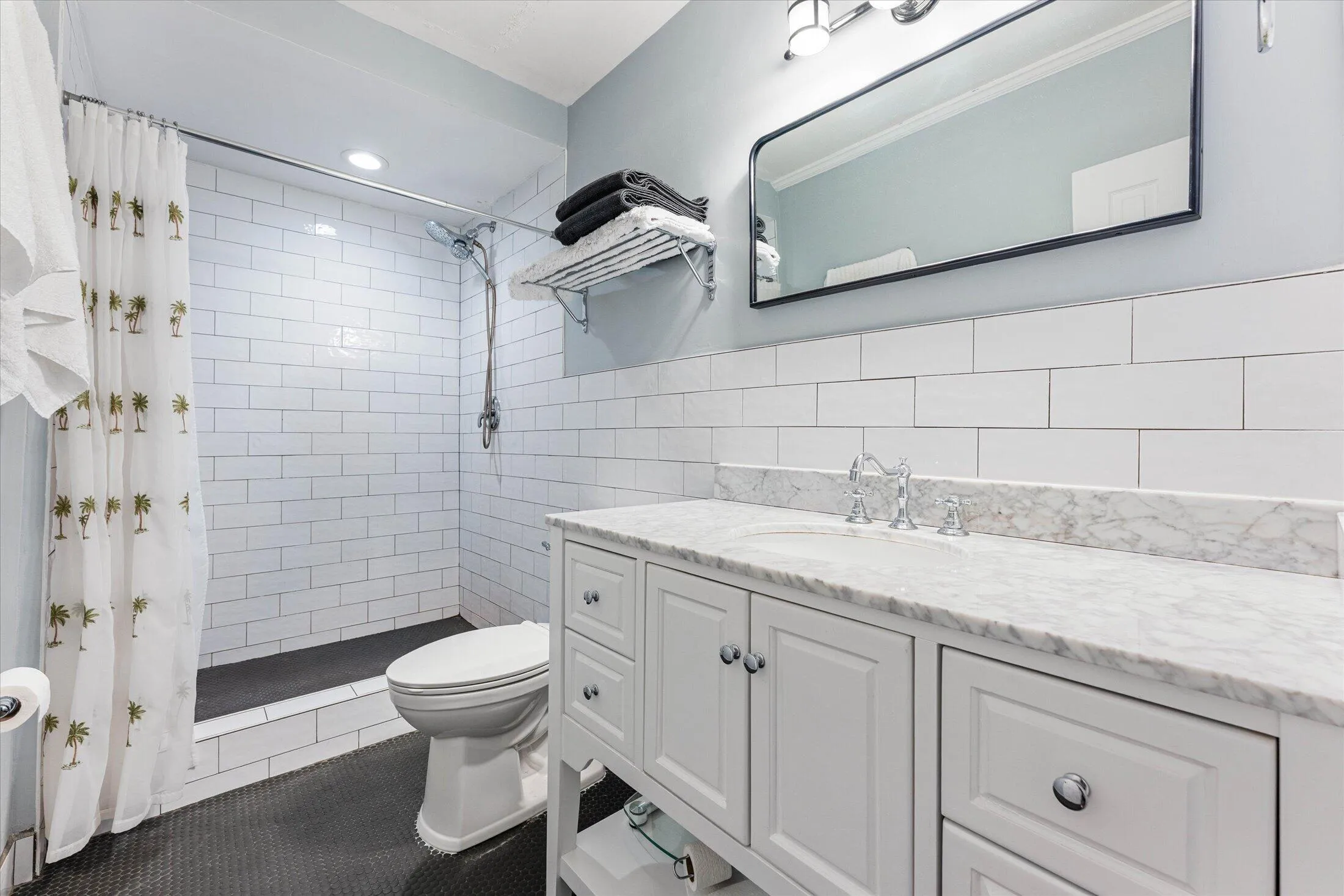 Bathroom featuring a white subway tile shower surround and a white vanity with a marble countertop