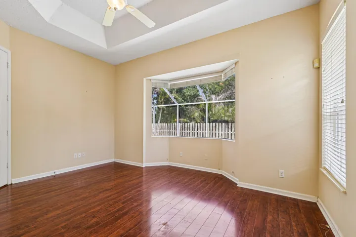 Bedroom featuring wood-finish flooring, a tray ceiling with a ceiling fan, and a large bay window overlooking a fenced area