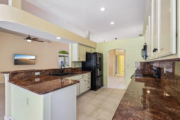 Kitchen featuring extensive stone countertops, white cabinetry, a black sink with a matte black faucet, and tile flooring