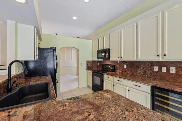 Kitchen featuring extensive perimeter cabinetry, durable countertops with integrated backsplash, a black undermount sink with a gooseneck faucet, black appliances, and a built-in beverage refrigerator
