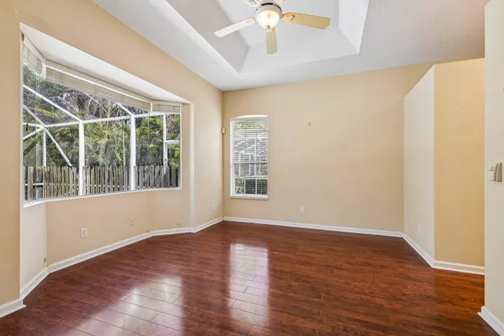 Spacious room featuring rich wood-finish flooring, a tray ceiling with a ceiling fan, and bay windows