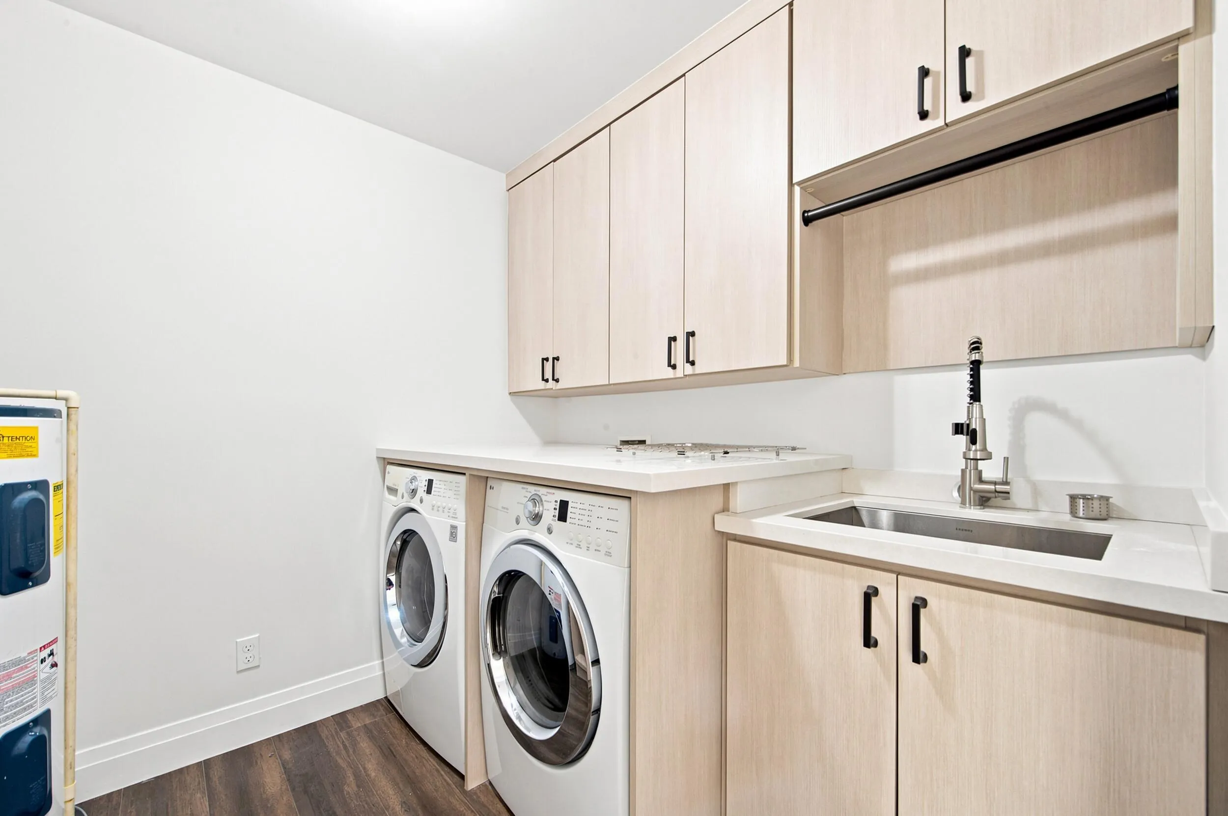Laundry room featuring wood-finish flooring, white walls, and light wood-tone cabinetry with black hardware