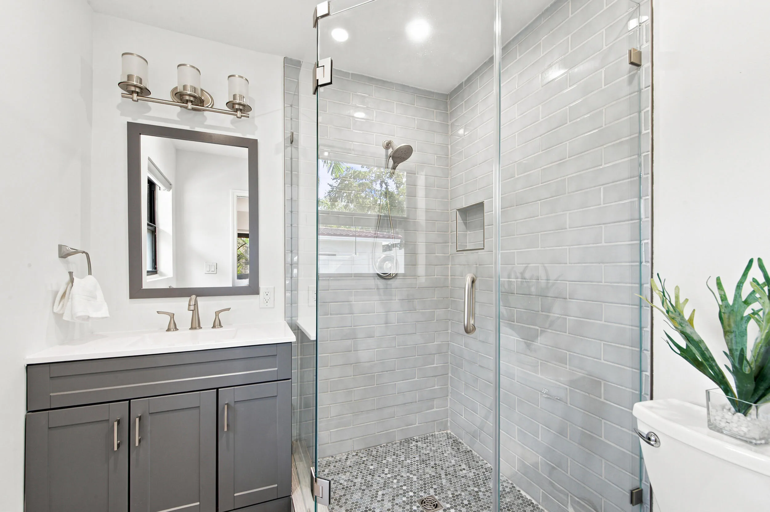 Modern bathroom featuring a frameless glass shower enclosure with subway tile surround and pebble flooring