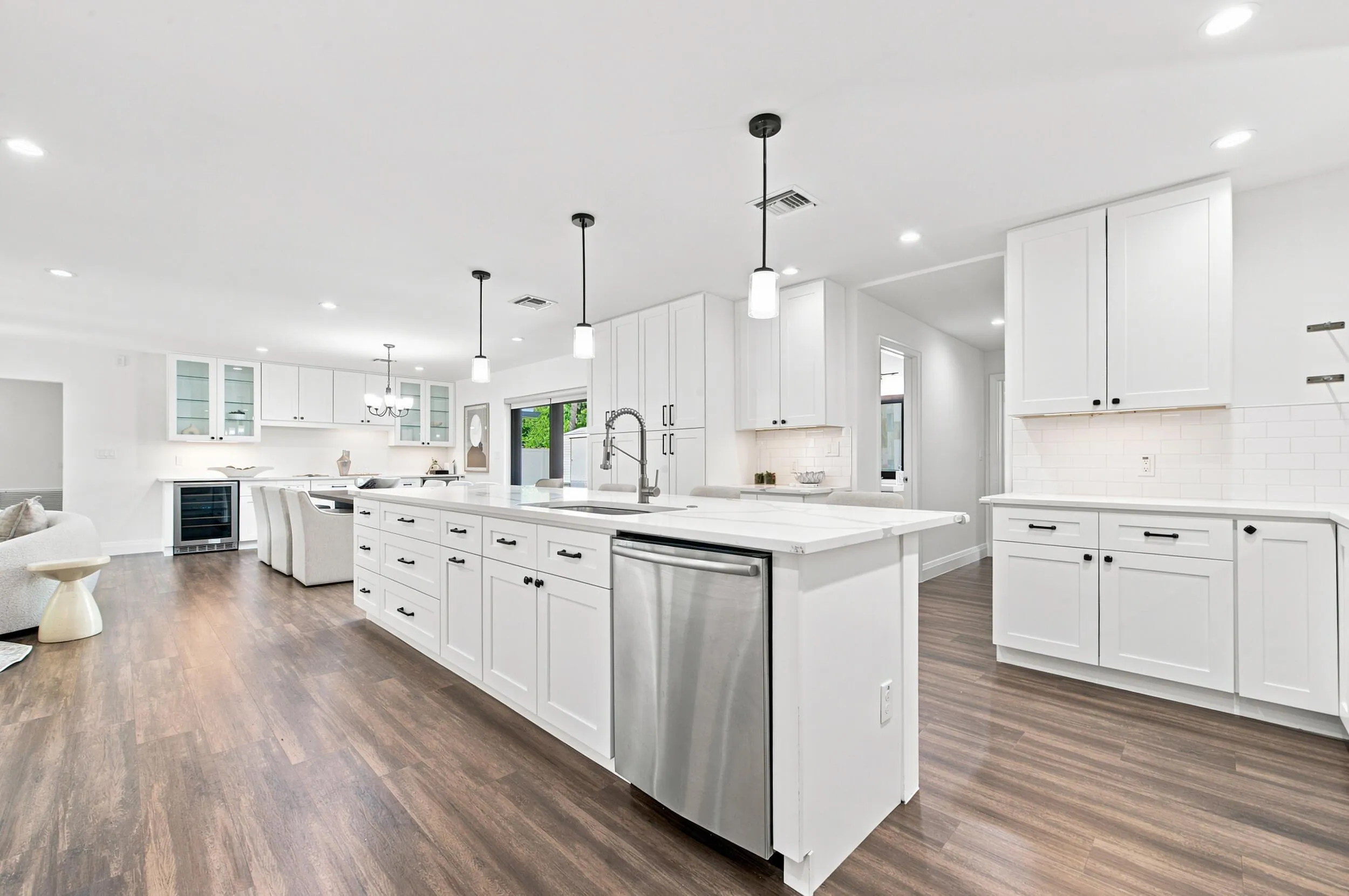 Expansive kitchen featuring a large central island with integrated sink, white cabinetry, stainless steel appliances, wood-finish flooring, and recessed lighting