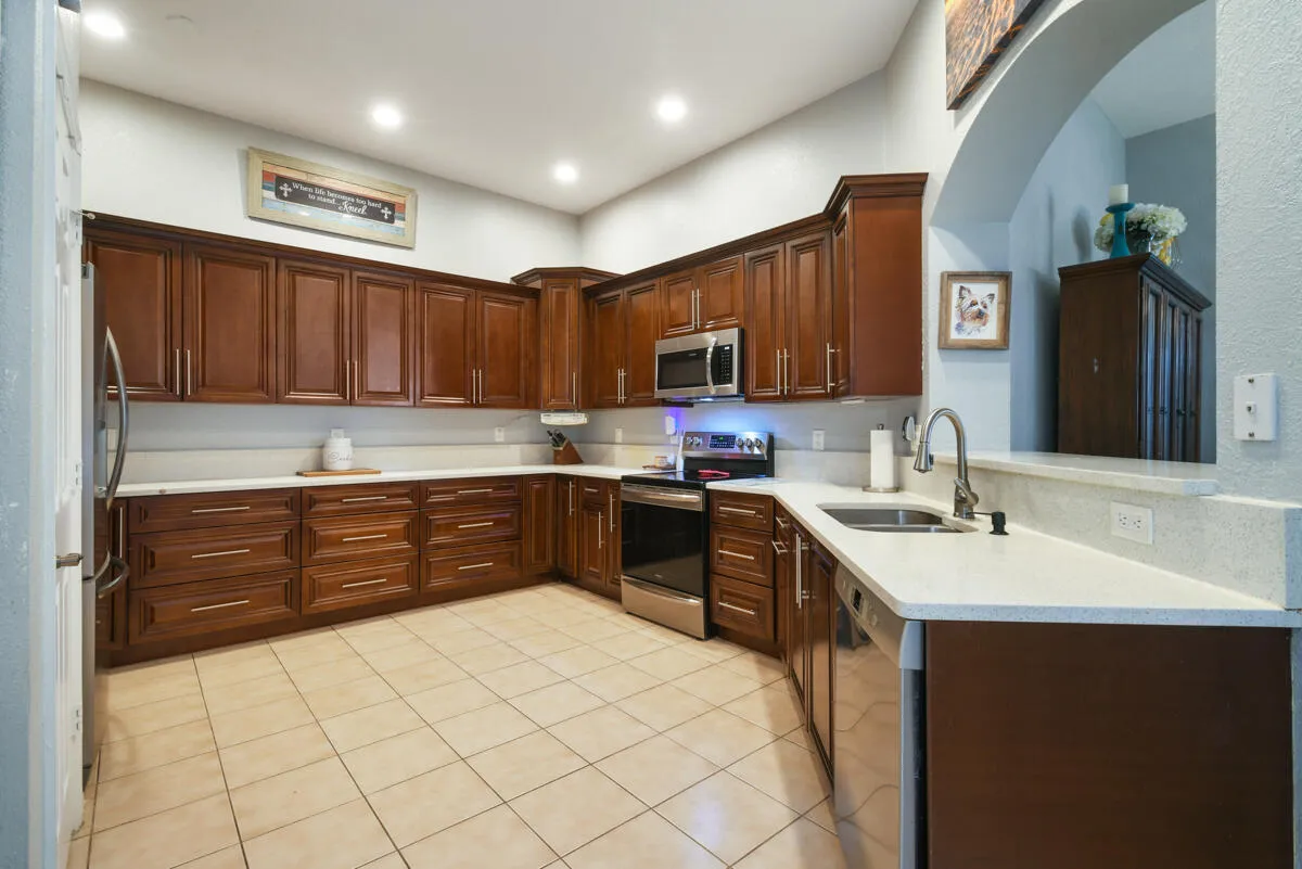 Kitchen featuring extensive wood cabinetry, light-toned countertops, stainless steel appliances, and tile flooring