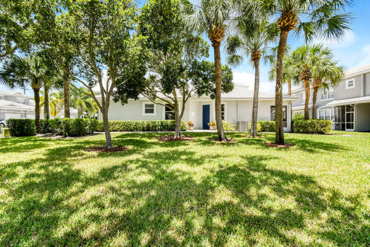 Expansive green lawn framed by mature trees and palm trees, featuring a light-colored exterior with a prominent blue entry door