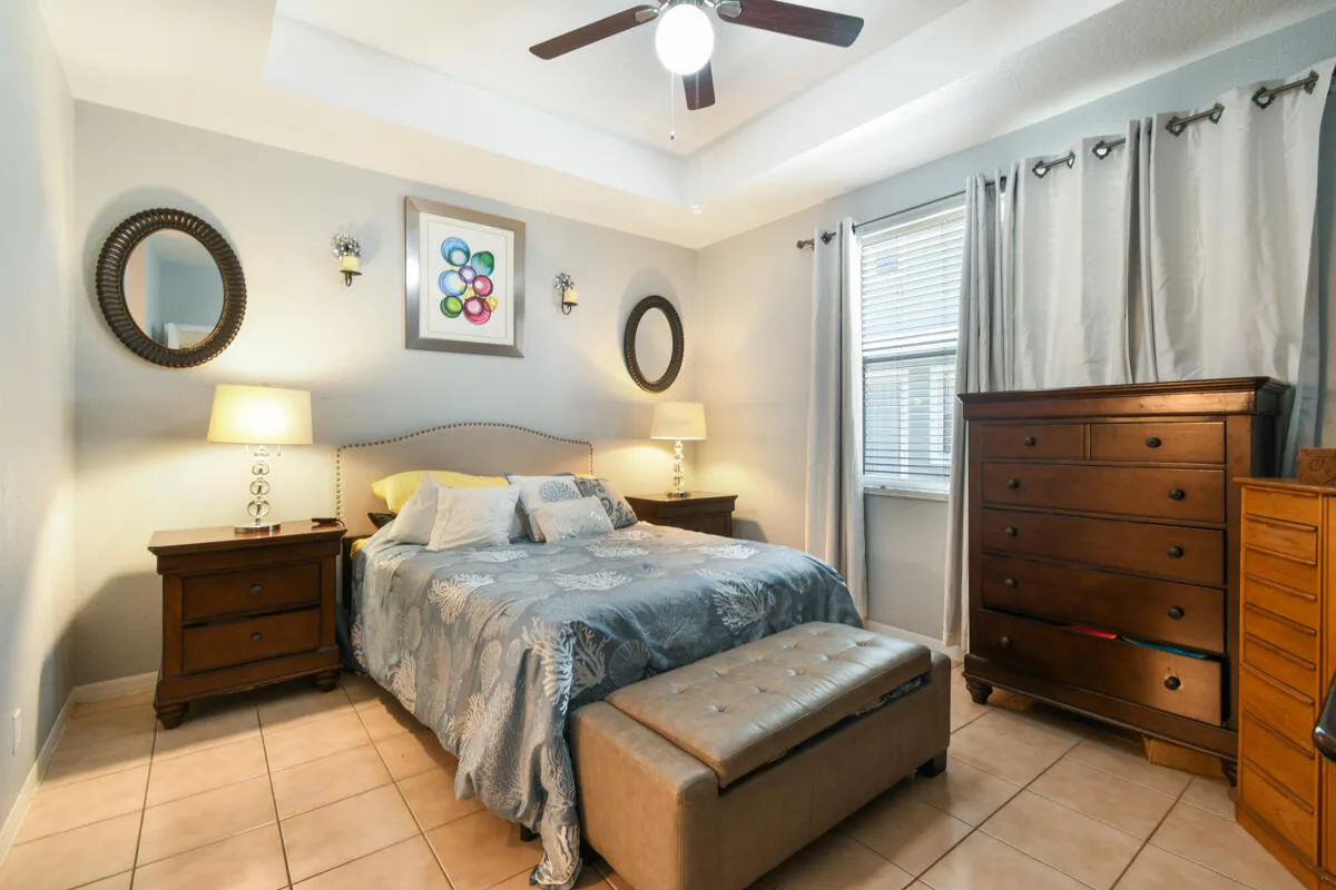 Bedroom featuring a tray ceiling with a ceiling fan, recessed window with blinds, and tile flooring