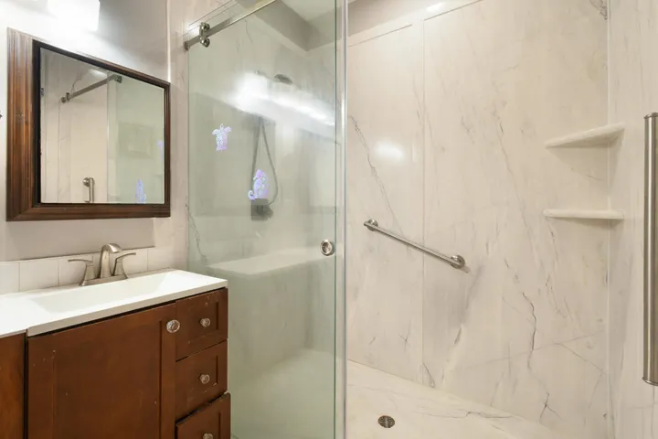 Bathroom featuring a walk-in shower with a glass enclosure, white marble-look shower walls, and built-in shelving