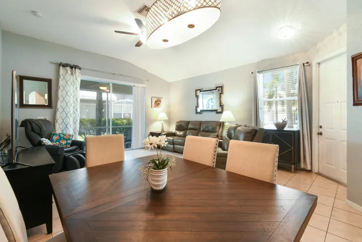 Open concept living area featuring vaulted ceilings, a wood-finish dining table, ceramic tile flooring, and sliding glass doors to the exterior