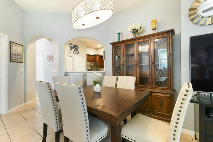 Dining area featuring vaulted ceilings, arched doorways, a built-in display cabinet with glass panels, and tile flooring