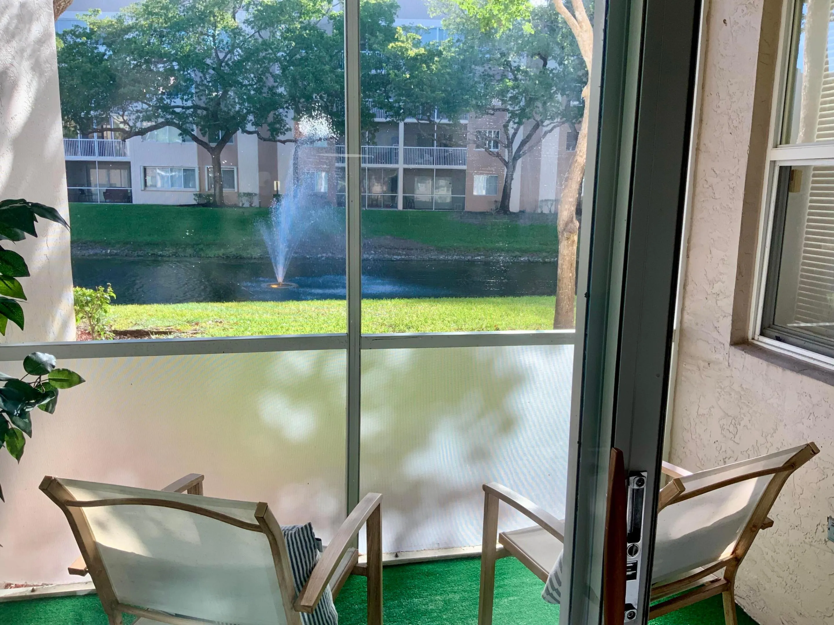 Screened patio with ceiling fan and artificial turf overlooking pond with lighted fountain.