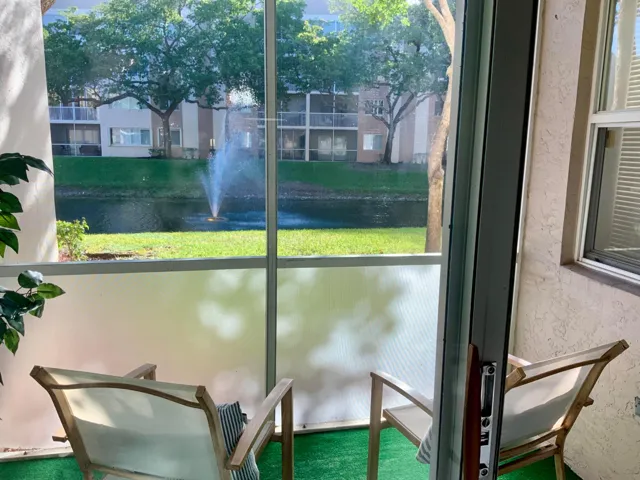 Screened patio with ceiling fan and artificial turf overlooking pond with lighted fountain.