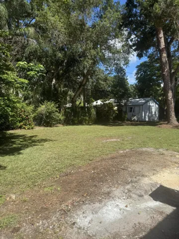 Expansive grassy area with mature trees and a detached storage shed