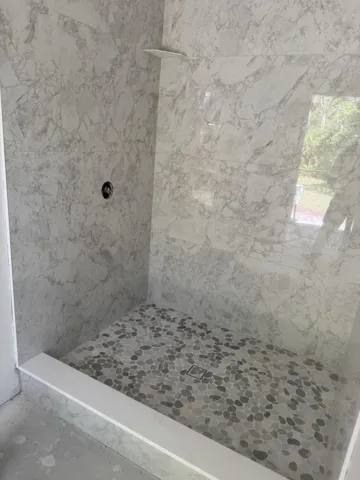 Shower stall featuring large format white marble-patterned wall tiles and a grey pebble-tile floor