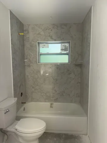 Bathroom featuring a white bathtub, toilet, and marble-look tile surround