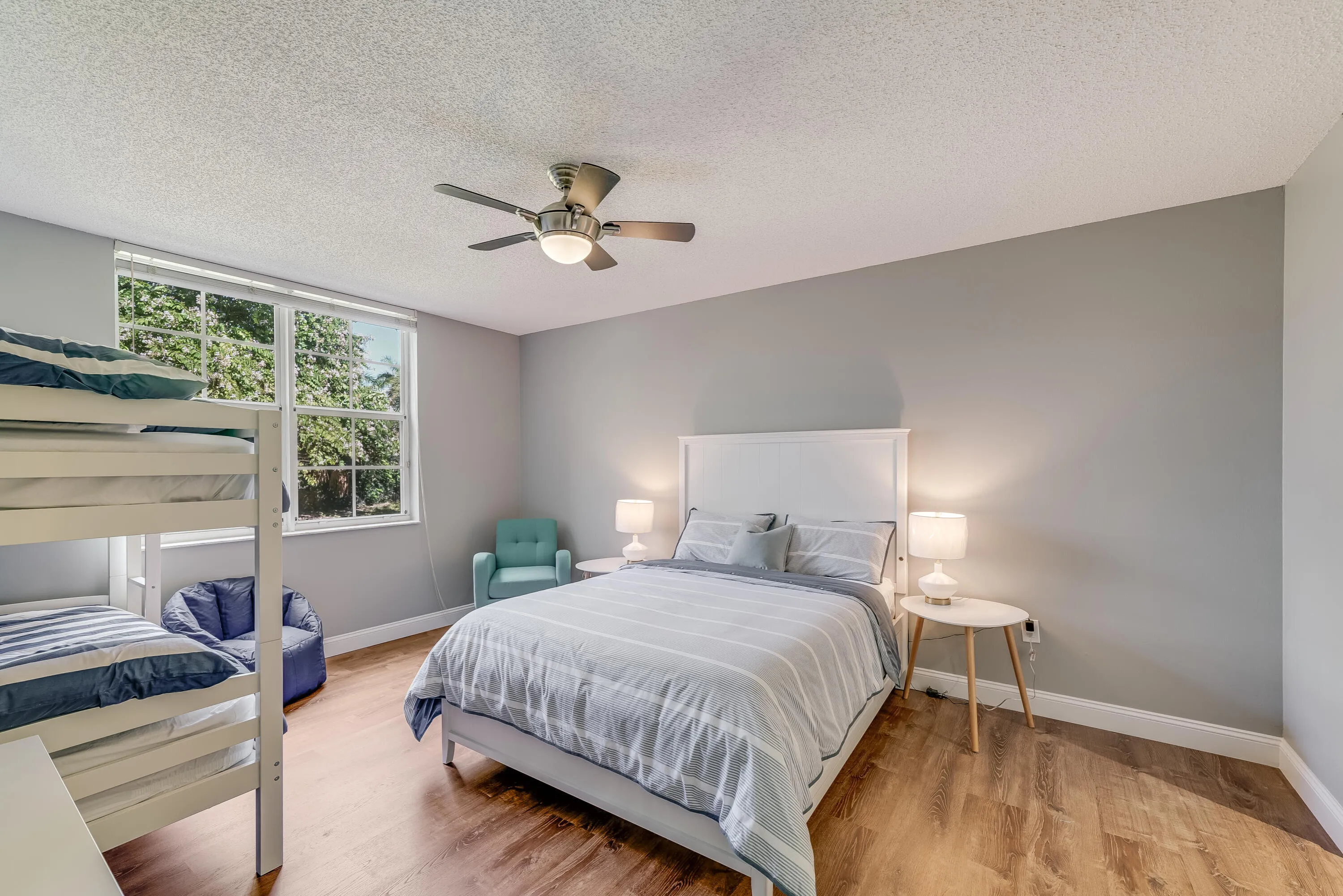 Spacious room featuring wood-finish flooring, a large window, a ceiling fan with integrated lighting, and neutral wall tones