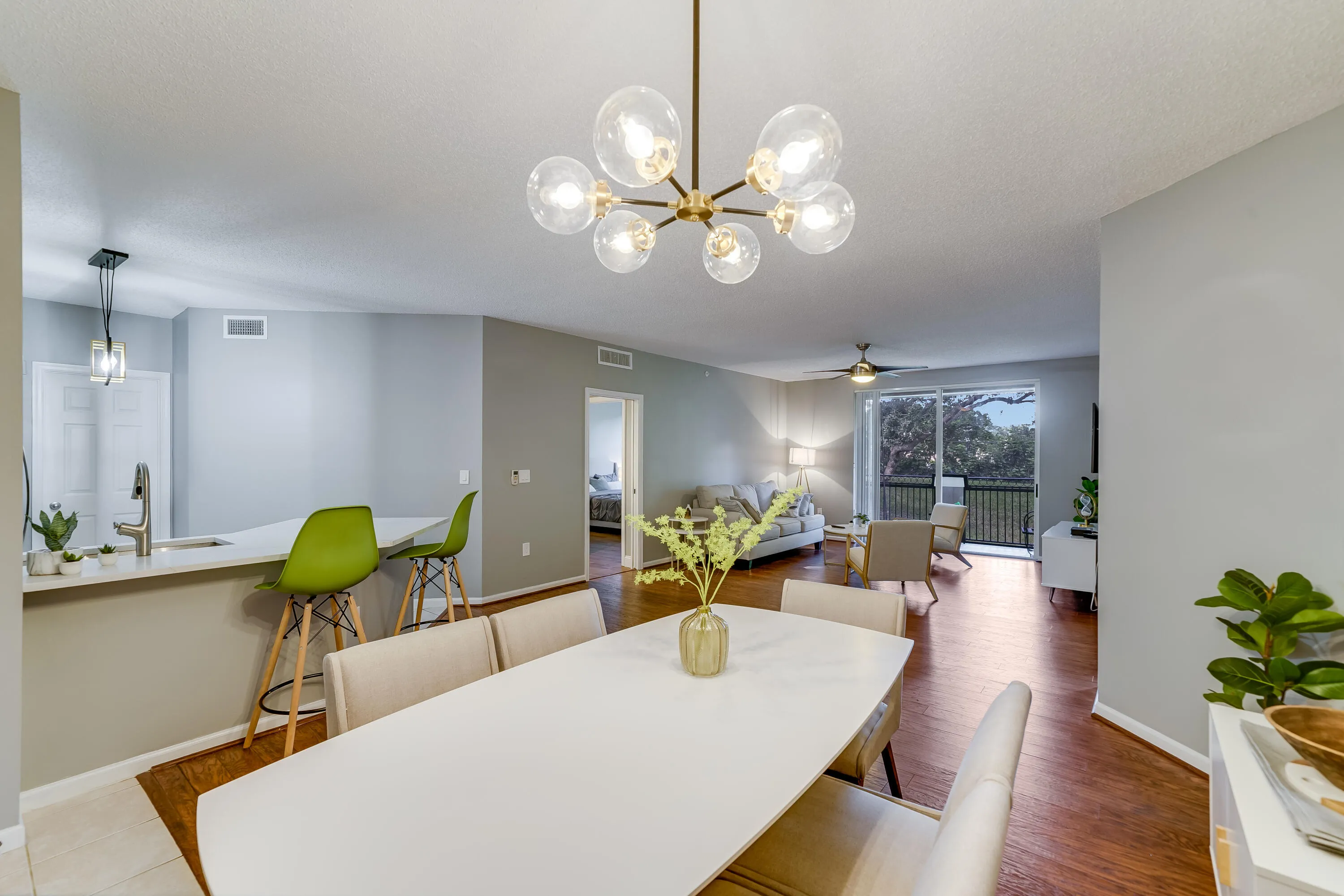 Open-concept living space featuring wood-finish flooring, a modern chandelier, and a sliding glass door to a balcony