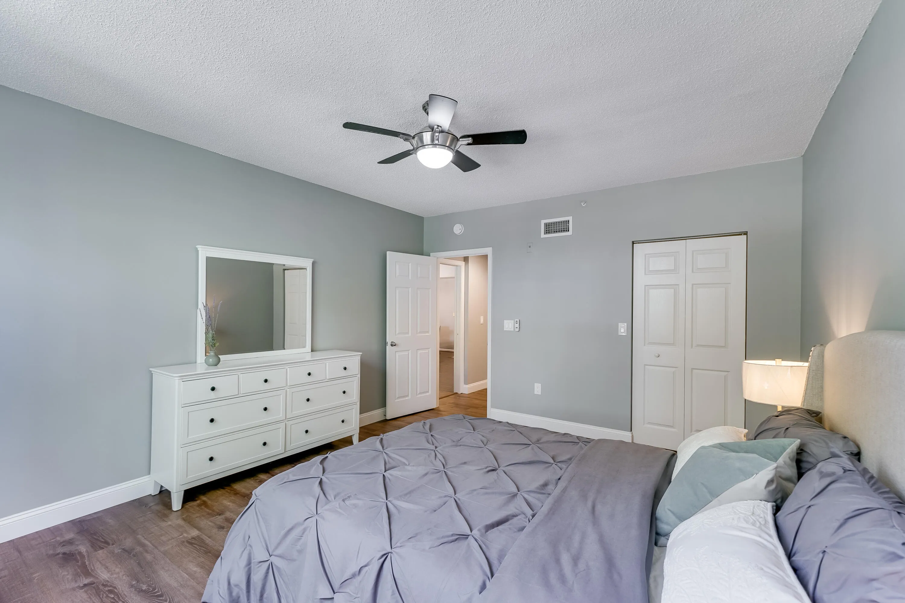 Bedroom featuring neutral gray walls, wood-finish flooring, a ceiling fan with integrated lighting, and white bi-fold closet doors
