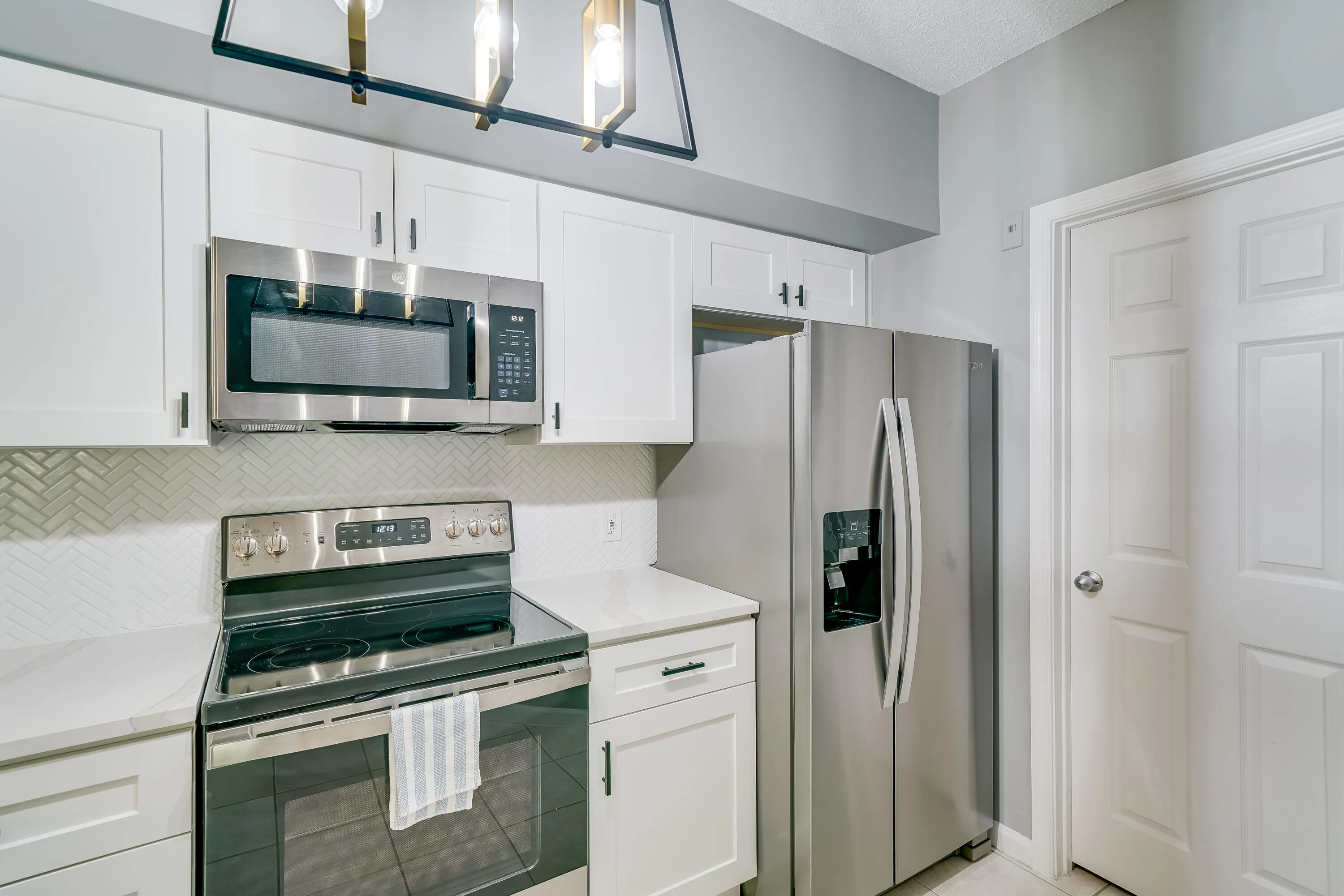 Kitchen featuring white shaker cabinetry, stainless steel appliances, white countertops, and a herringbone tile backsplash