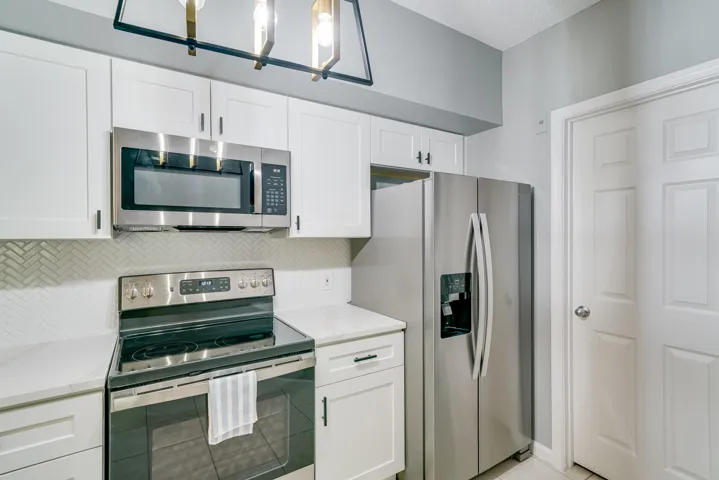 Kitchen featuring white shaker cabinetry, stainless steel appliances, white countertops, and a herringbone tile backsplash