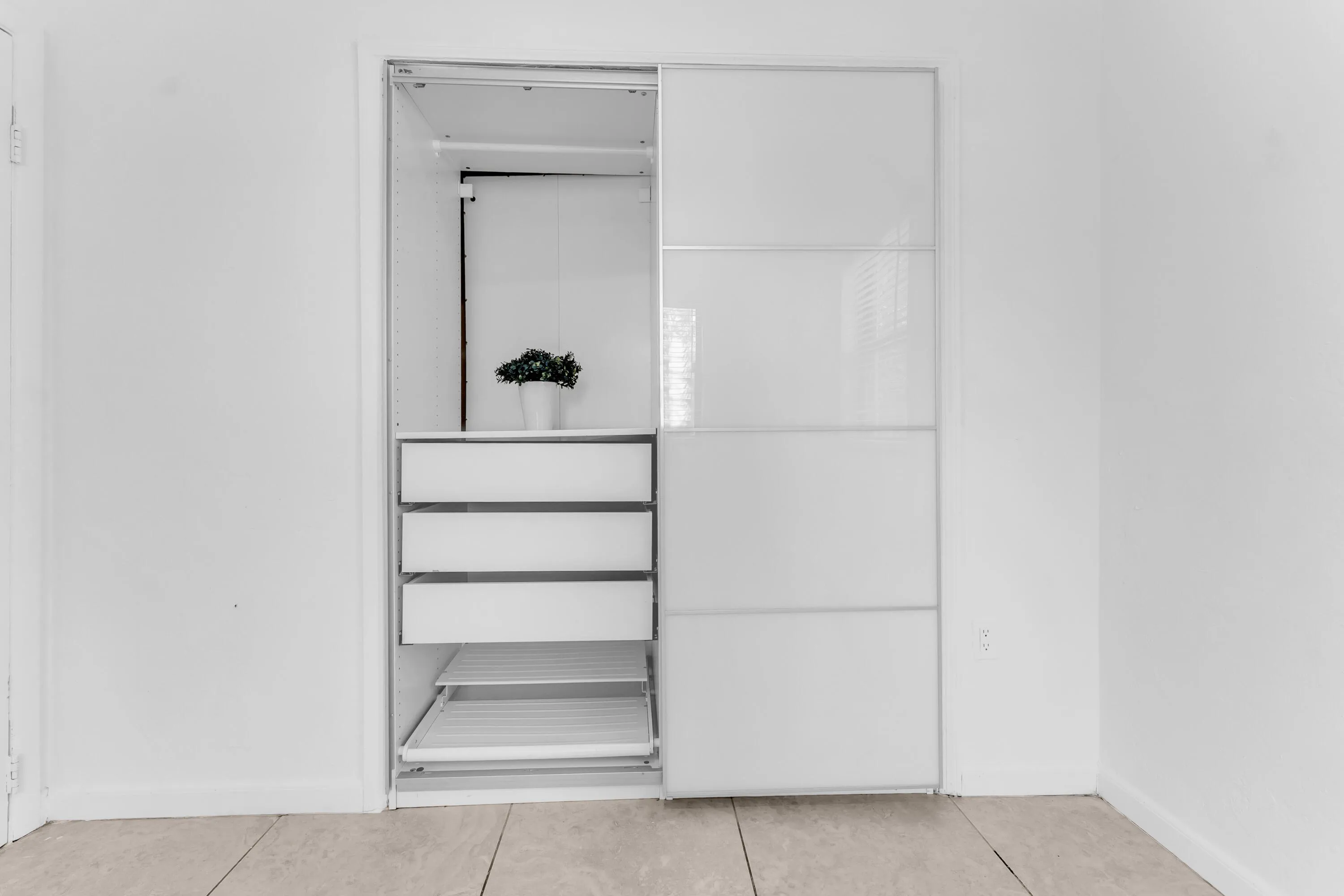 Built-in closet system featuring white sliding doors with frosted glass panels, an internal hanging rod, multiple drawers, and pull-out shelving