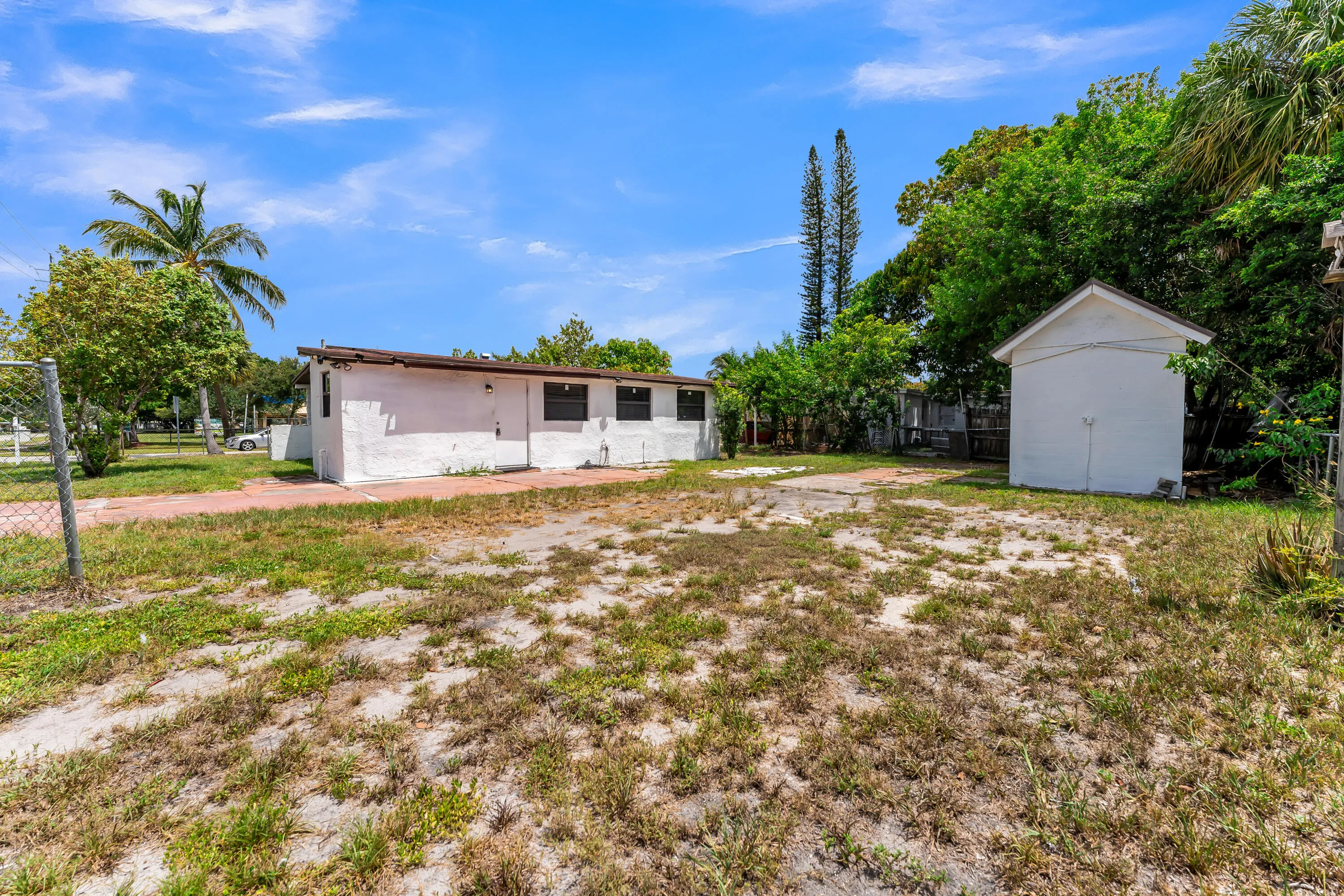Expansive rear yard featuring a detached storage shed, mature trees, and a perimeter fence