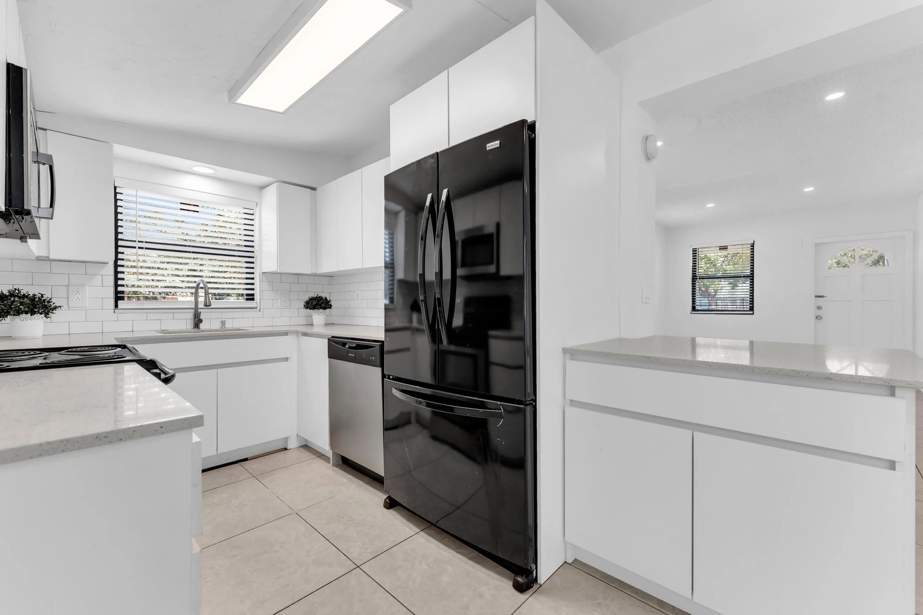 Modern kitchen featuring white cabinetry, light-toned countertops, a full suite of appliances, subway tile backsplash, and tile flooring