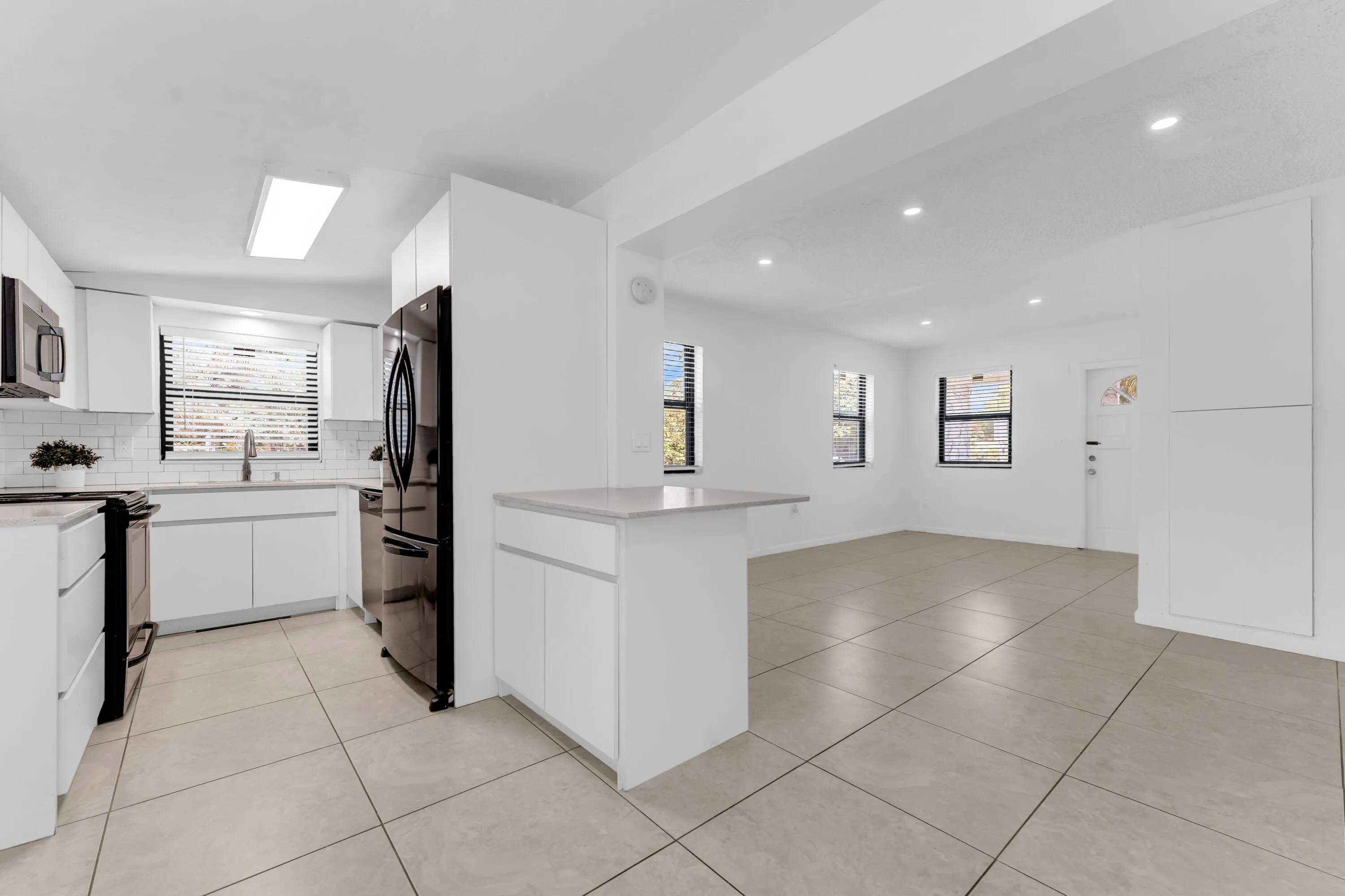 Open-concept living area featuring a modern kitchen with white cabinetry, stainless steel appliances, and a subway tile backsplash